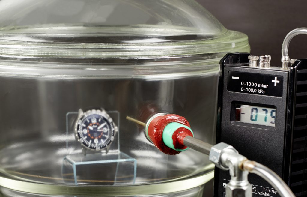 Differenzdruckprüfung in einem Vakuumexsikkator. Eine Fliegeruhr nach DIN 8330 muss mehrtausendfache Druckwechselbelastungen aushalten.